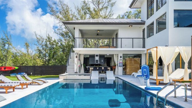 A modern two-story house with a swimming pool, outdoor seating, and a covered area with lounge chairs. - Heated Pool • Hot Tub • Theater • Waterfront (Key Largo)