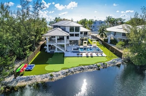 A two-story house with a swimming pool, surrounded by greenery and a body of water.