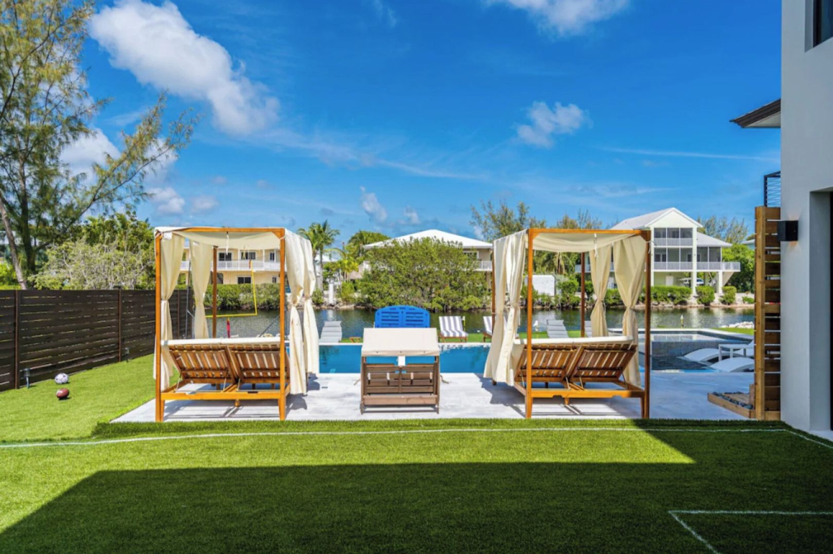 A backyard with a swimming pool, two wooden gazebos, a lawn, and a house in the background.