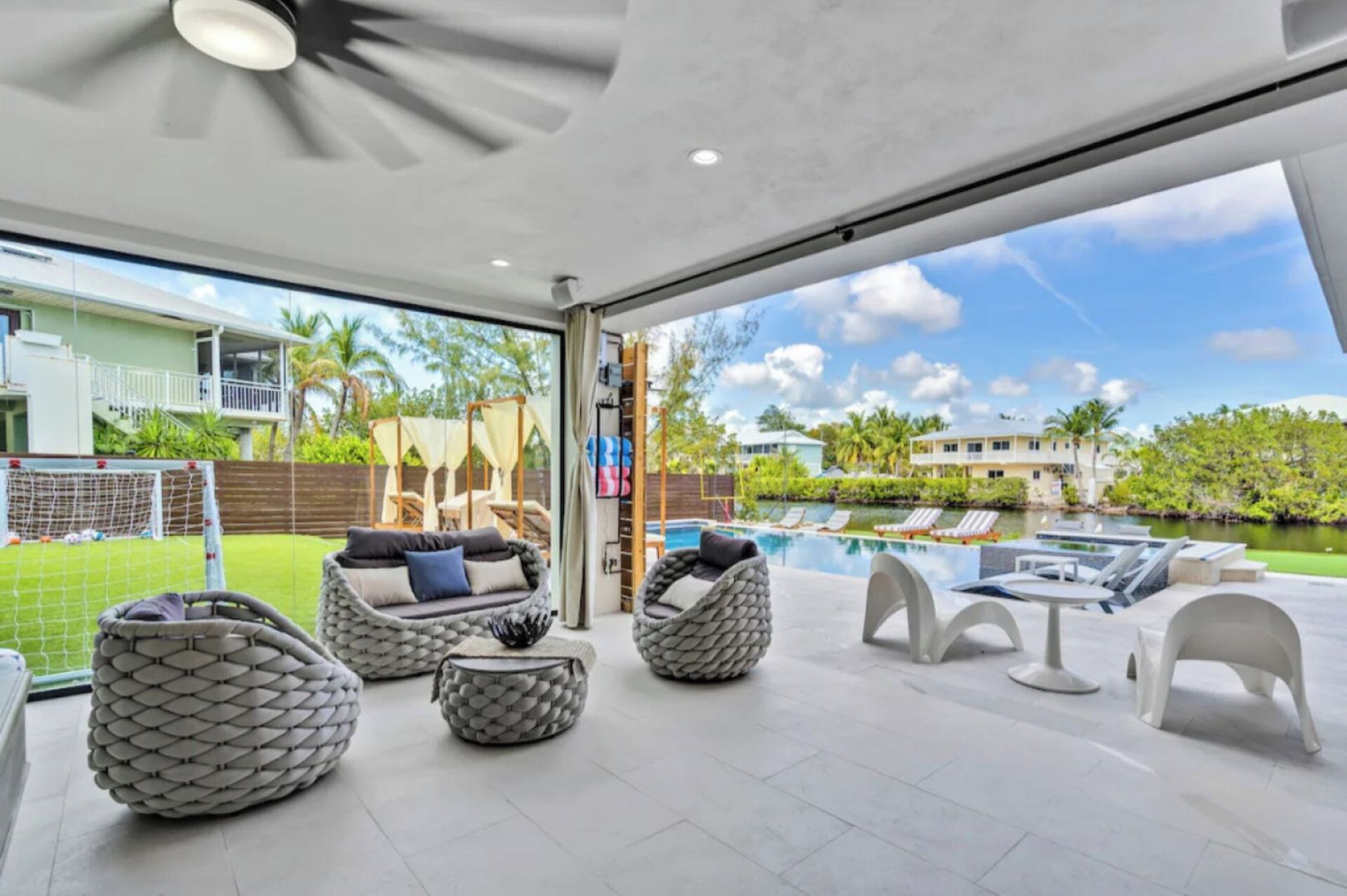 A modern outdoor living space with wicker furniture, a pool, and a view of the surrounding neighborhood.