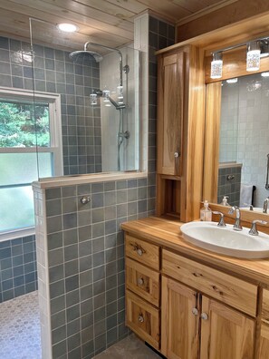 Ein Badezimmer mit Dusche, Holzschränken, einem Waschbecken und einem großen Spiegel.
