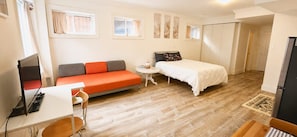 A compact room with a bed, a sofa, a small table, and a desk with a computer.