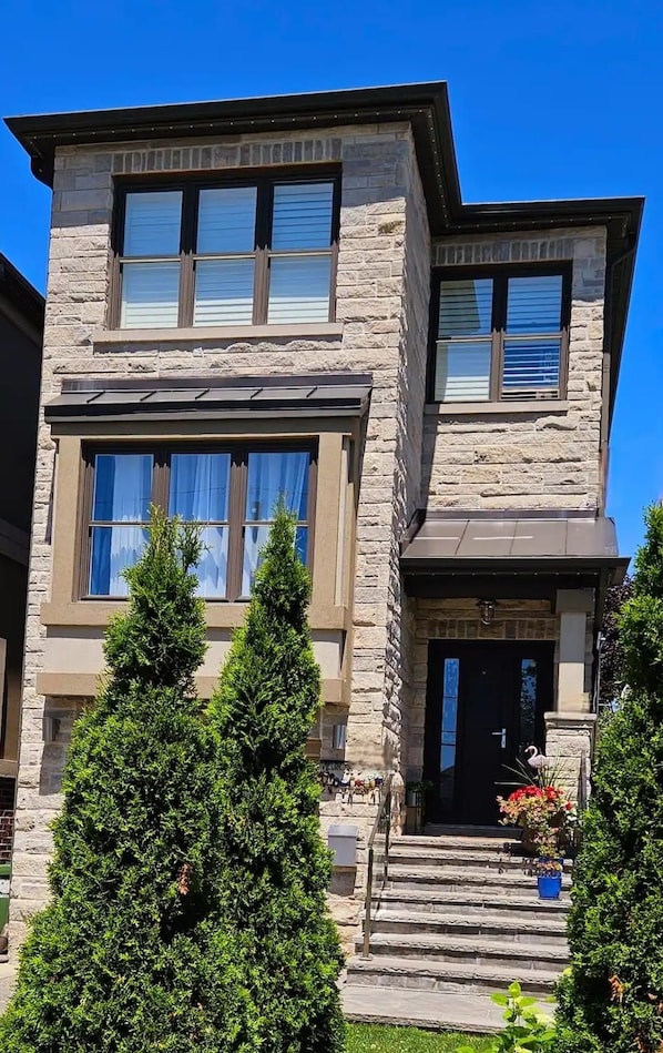 A two-story house with a stone facade, large windows, and a front porch with steps leading to the entrance.
