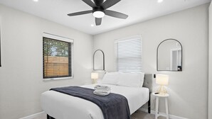Un dormitorio moderno con una cama, dos lámparas de noche, un ventilador de techo y una ventana con persianas.