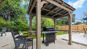 Un espacio al aire libre con patio, una pérgola, una parrilla y arreglos de asientos.