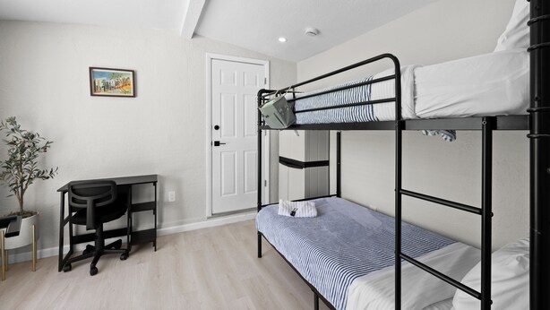 Una cama litera con escritorio y silla, una puerta y una planta en maceta.