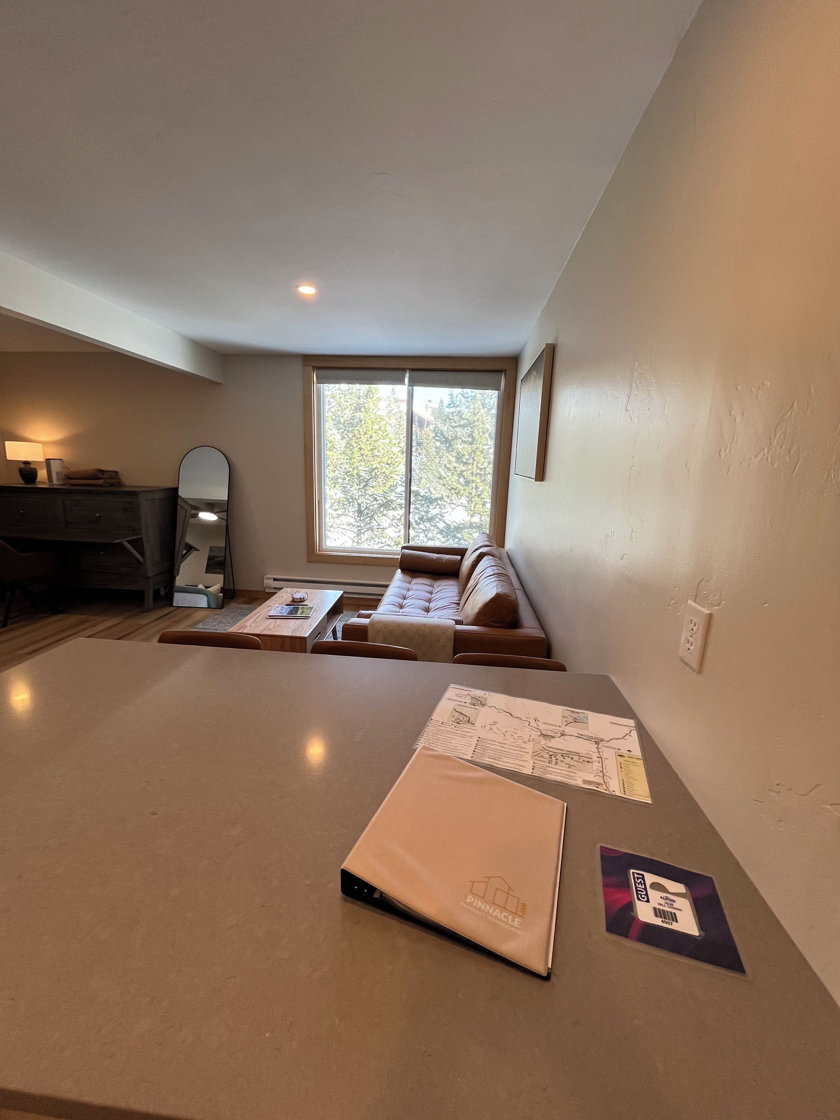 A room with a large window, a sofa, a table, and a desk with papers.