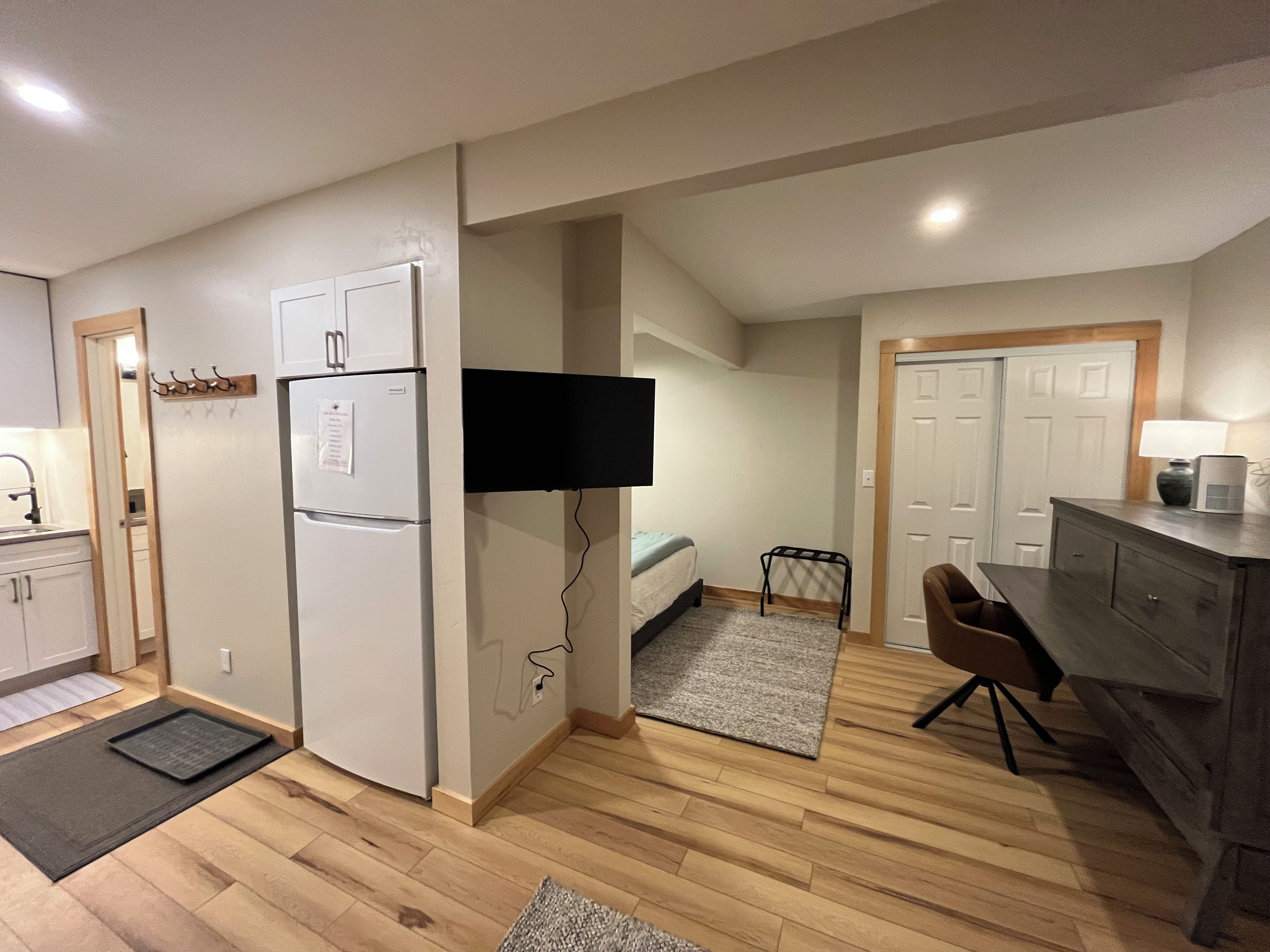 A compact kitchen with a refrigerator, a microwave, and a flat-screen TV mounted on the wall.