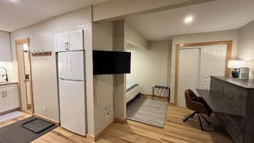 A compact kitchen with a refrigerator, a microwave, and a flat-screen TV mounted on the wall.