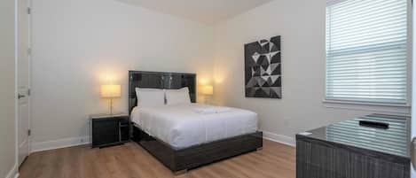 Quarto com cama, duas mesas de cabeceira, uma obra de arte na parede e uma janela com persianas.