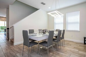 A dining area with a glass table, grey upholstered chairs, and a modern pendant light. - 14 Min to Disney, Modern Home for 10 Guests (Kissimmee)