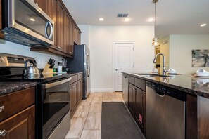 A modern kitchen with stainless steel appliances, wooden cabinets, and a granite countertop. - 14 Min to Disney, Modern Home for 10 Guests (Kissimmee)