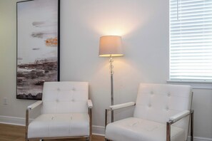 Zwei weiße Polsterstühle mit Metallgestellen, eine Stehlampe mit beiger Lampenschirm und ein großes Landschaftsbild an der Wand.