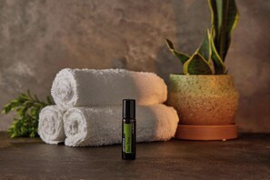 A bottle of doterra tea tree roll-on, a potted plant, and rolled white towels on a textured surface.