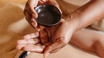 A person holding a small bowl, likely containing a skincare product, over their hand.