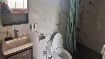 A bathroom with a toilet, sink, mirror, and shower.