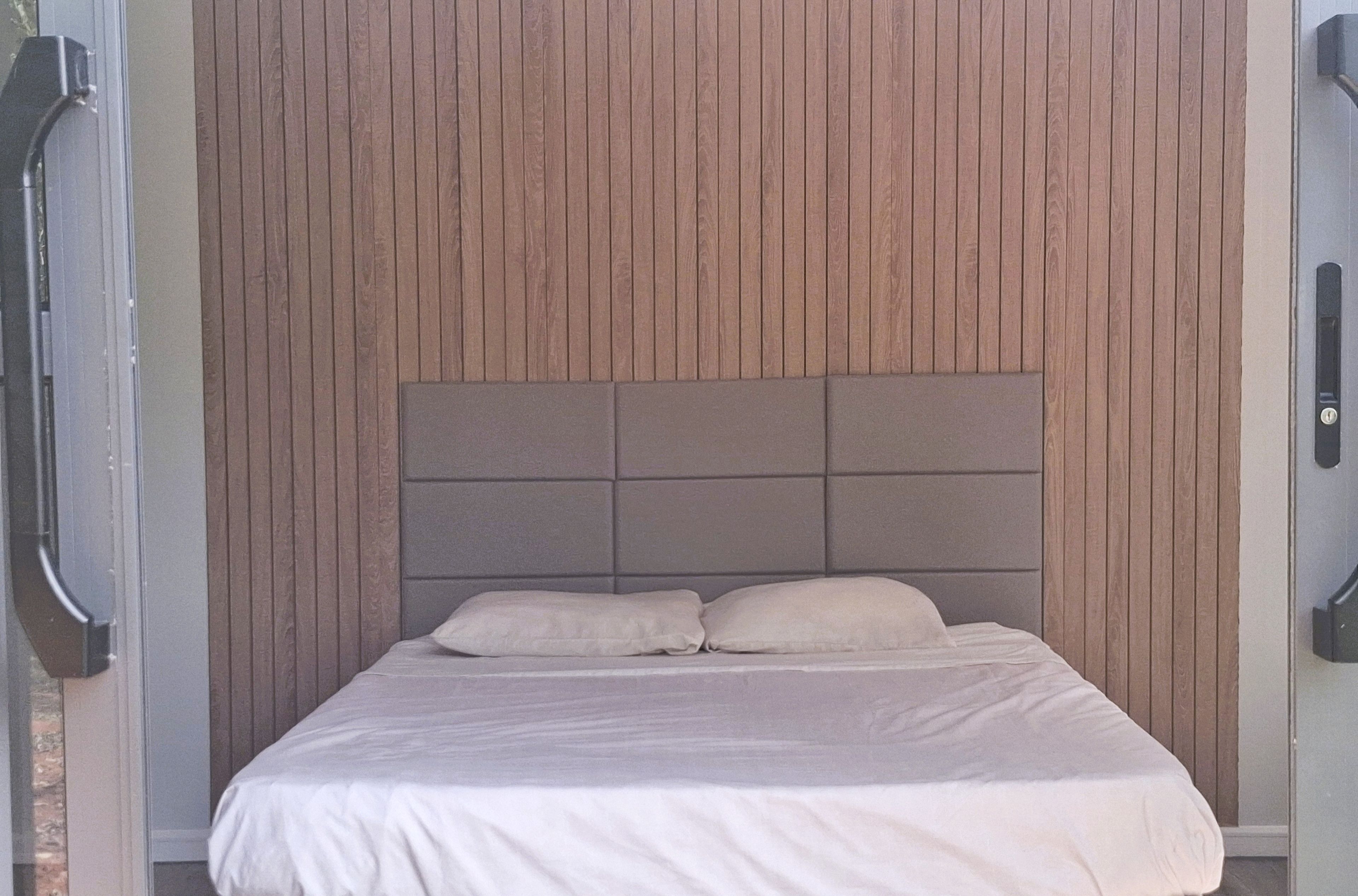A bed with a headboard against a wooden panel wall.