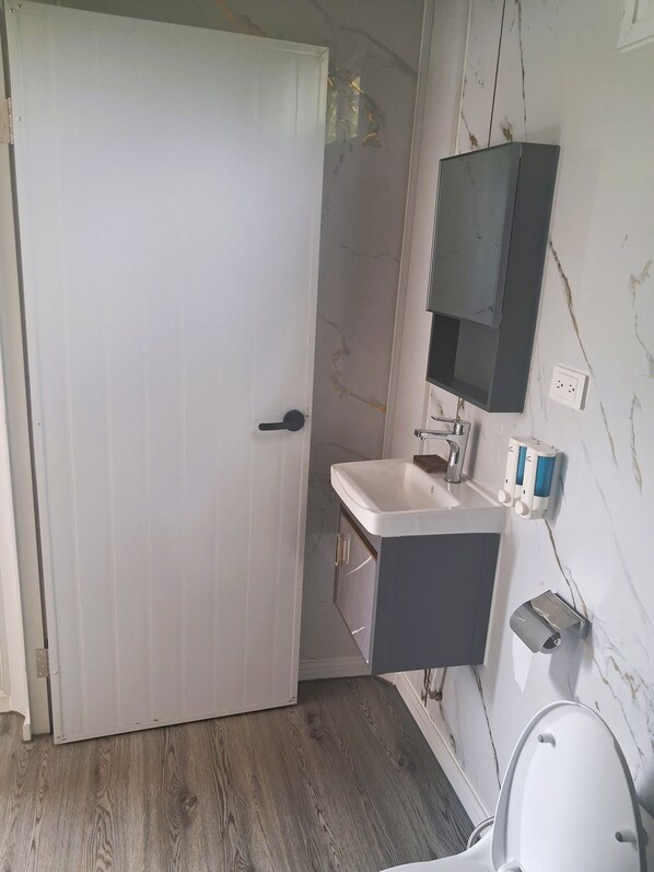 A bathroom with a white door, a sink, a mirror, and a toilet.