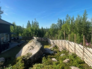 A building with a large rock in the foreground, surrounded by a forest and a wooden fence. - Family cabin near Trysilfjellet (Nybergsund)