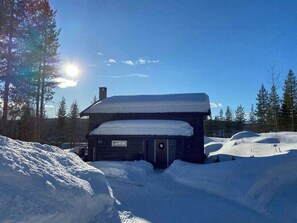 A wooden cabin with a snow-covered roof, surrounded by snow-covered ground and trees. - Family cabin near Trysilfjellet (Nybergsund)