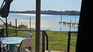 A patio area with a table and chairs, a colorful rug, and a view of a lake through a glass door.
