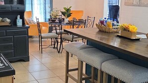 Ein Essbereich mit einem langen Holztisch, gepolsterten Barhocker und einer modernen Pendelleuchte.