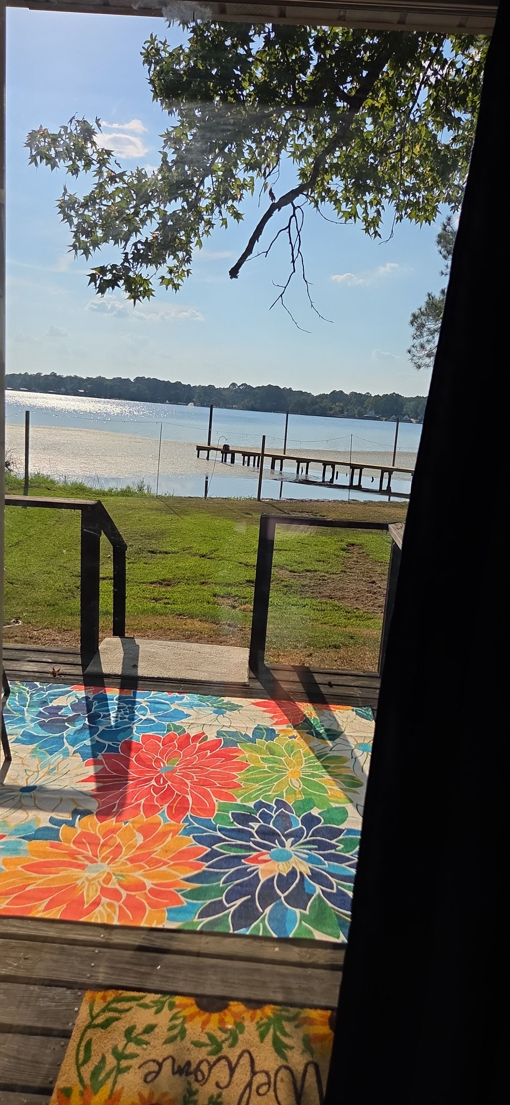 Eine Holzterrasse mit einer farbenfrohen Blumenmatte, einem Metallgeländer und Blick auf einen See.