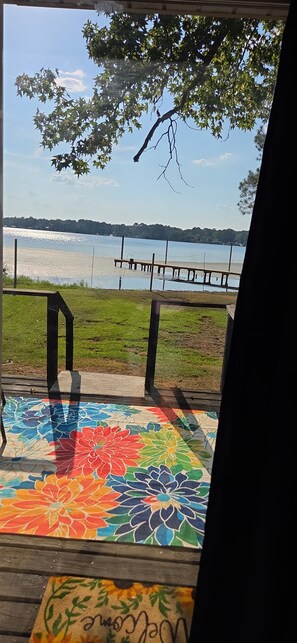 Una terraza de madera con un tapete floral de colores, barandilla metálica y vista a un lago.