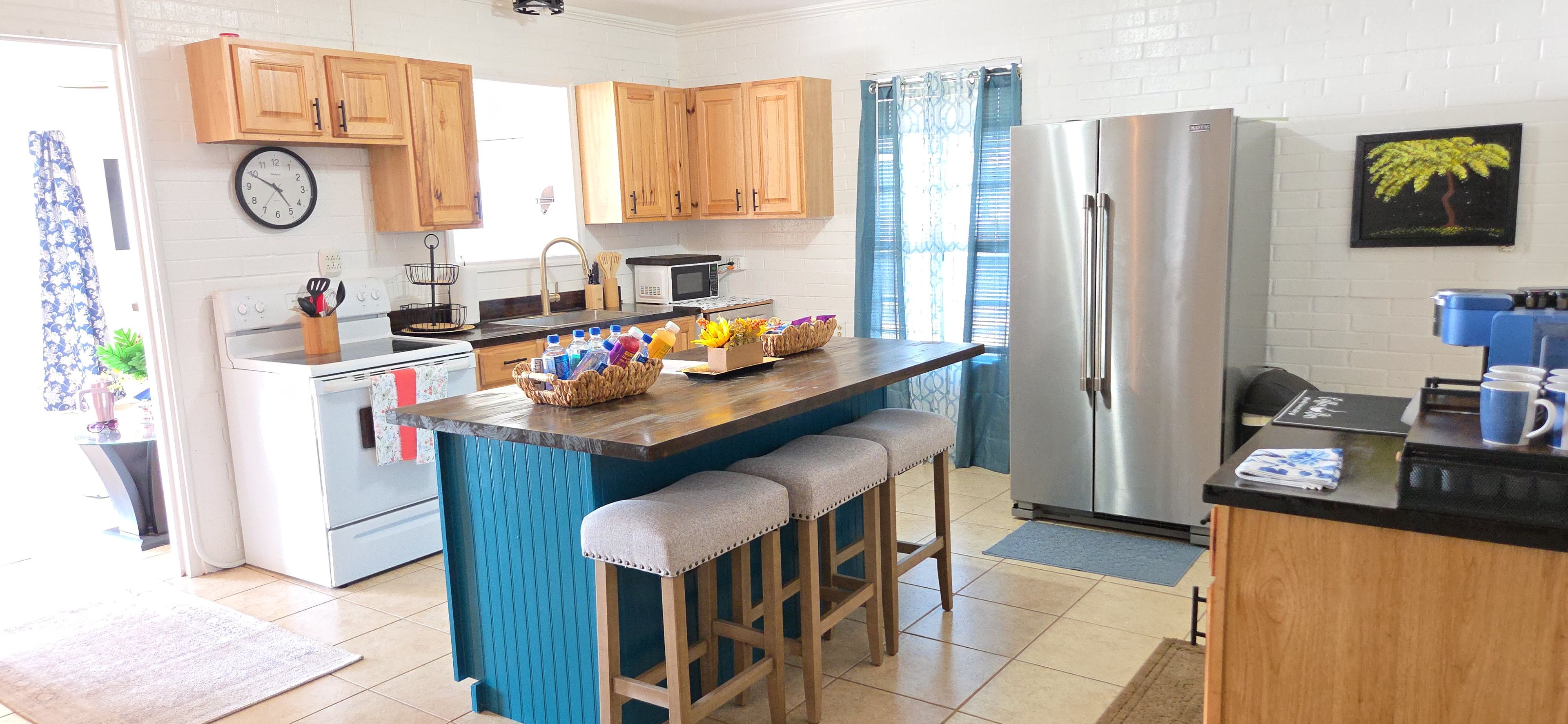 Una cocina moderna con armarios de madera, una isla central con taburetes, un refrigerador y un reloj en la pared.