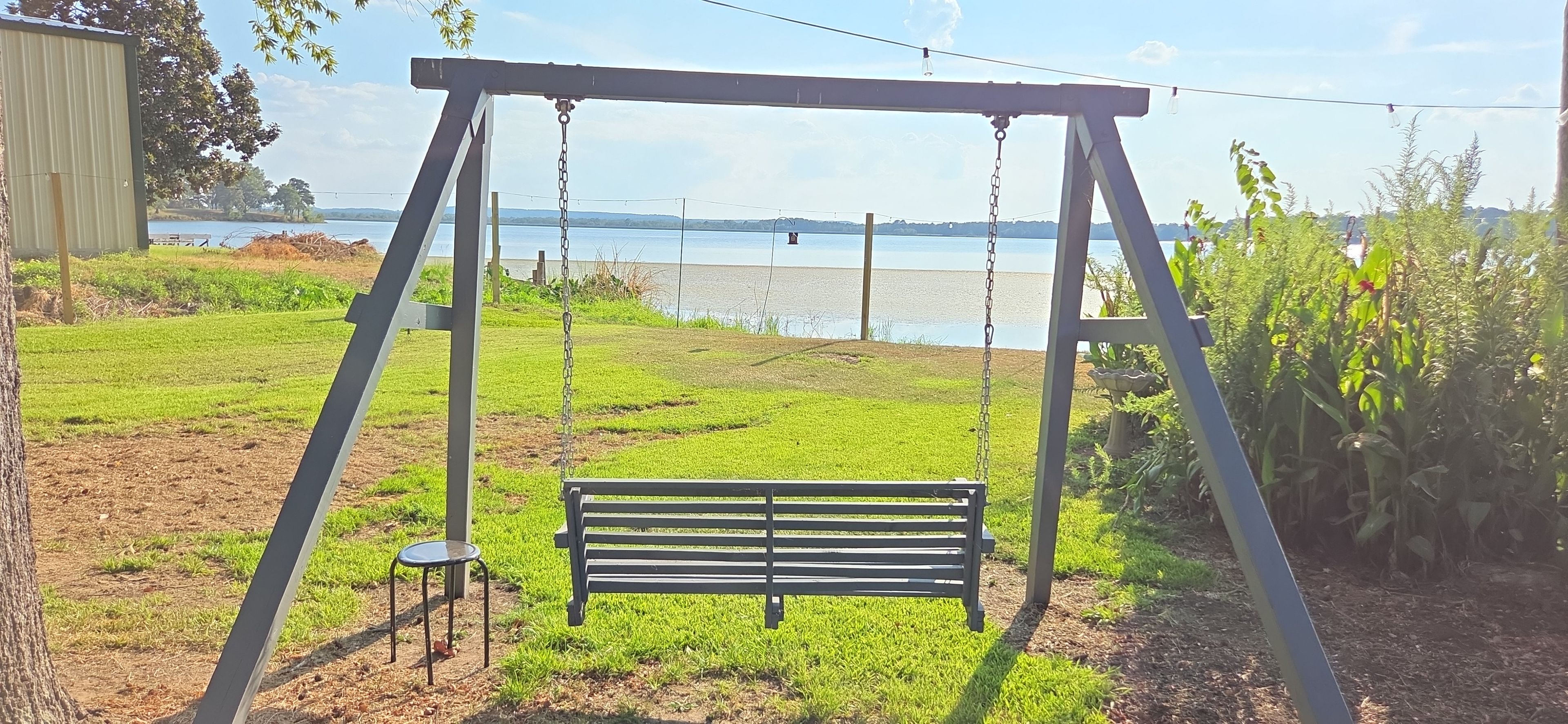 A swing set with a bench, a small stool, and a view of a lake.