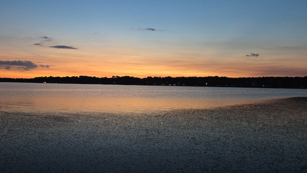 Ein Strand mit ruhiger Wasseroberfläche, die den Himmel spiegelt.