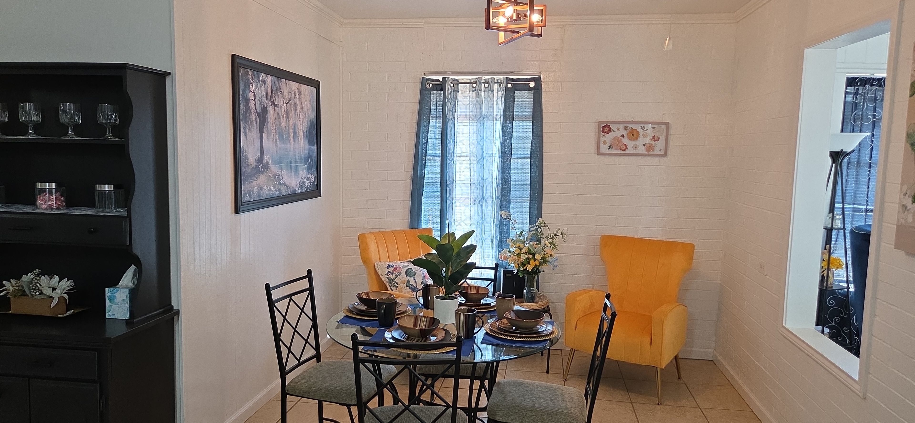 Un coin repas avec une table dressée pour quatre personnes, deux chaises, une bibliothèque et une fenêtre avec des rideaux.