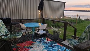Eine Terrasse mit blauem Tisch und Stühlen, einem Grill und Blick auf ein Gewässer.