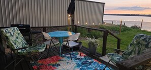 A deck with a blue table and chairs, a grill, and a view of a body of water.