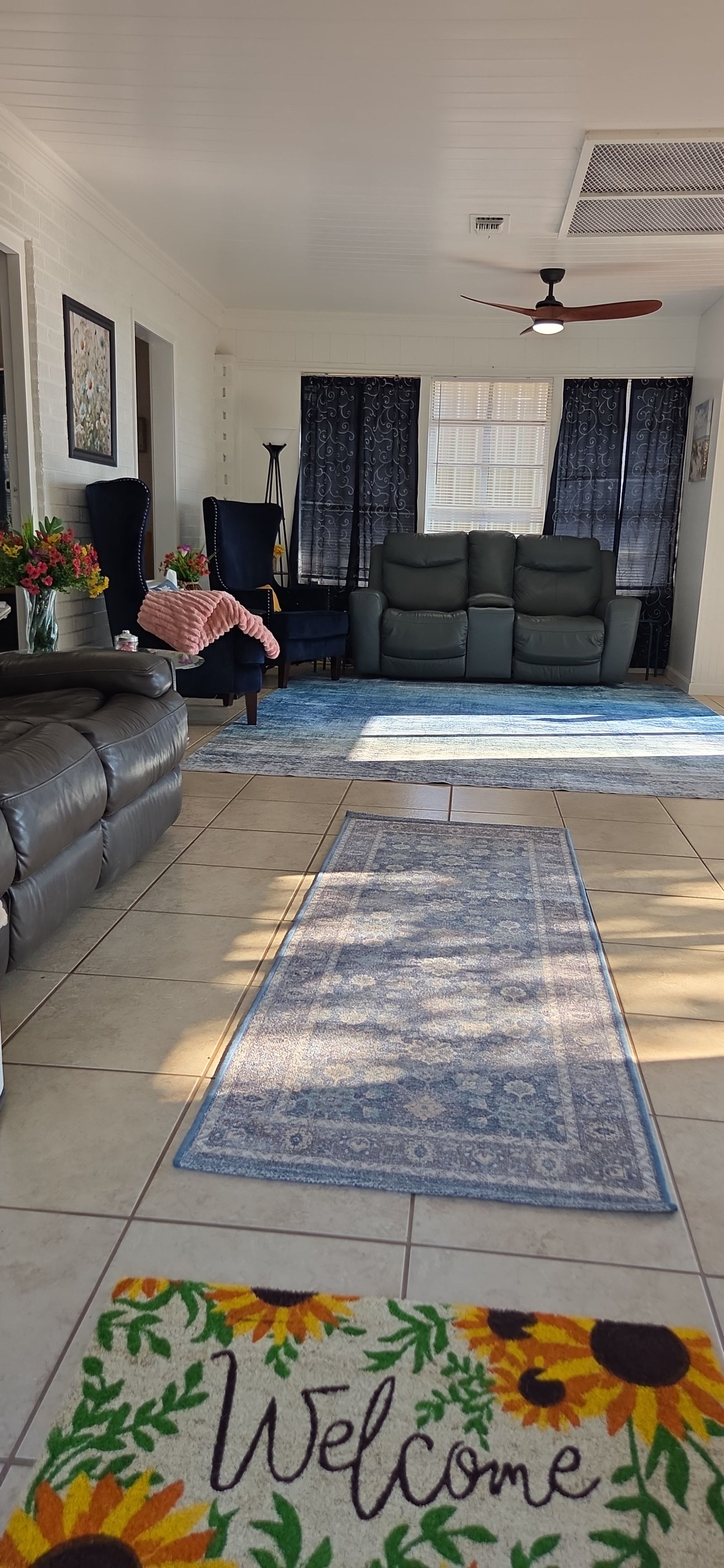 A living room with a sofa, a chair, a rug, and a welcome mat.