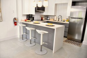 A modern kitchen with a central island, bar stools, a stainless steel refrigerator, and a fire extinguisher on the wall. - Elegant, ultra modern 1-bedroom studio apartment with AC in tranquil Ocho Rios (Ocho Rios)