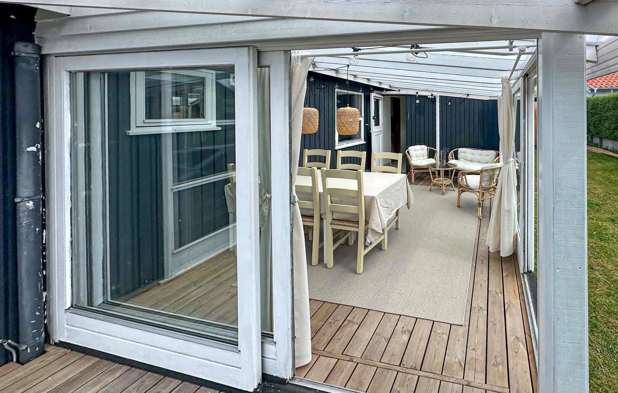 Een overdekt terras met een tafel en stoelen, een pergola erboven en een uitzicht op een huis op de achtergrond.