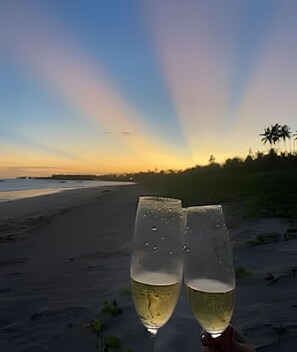 Dos copas de vino blanco en una playa con el atardecer de fondo.