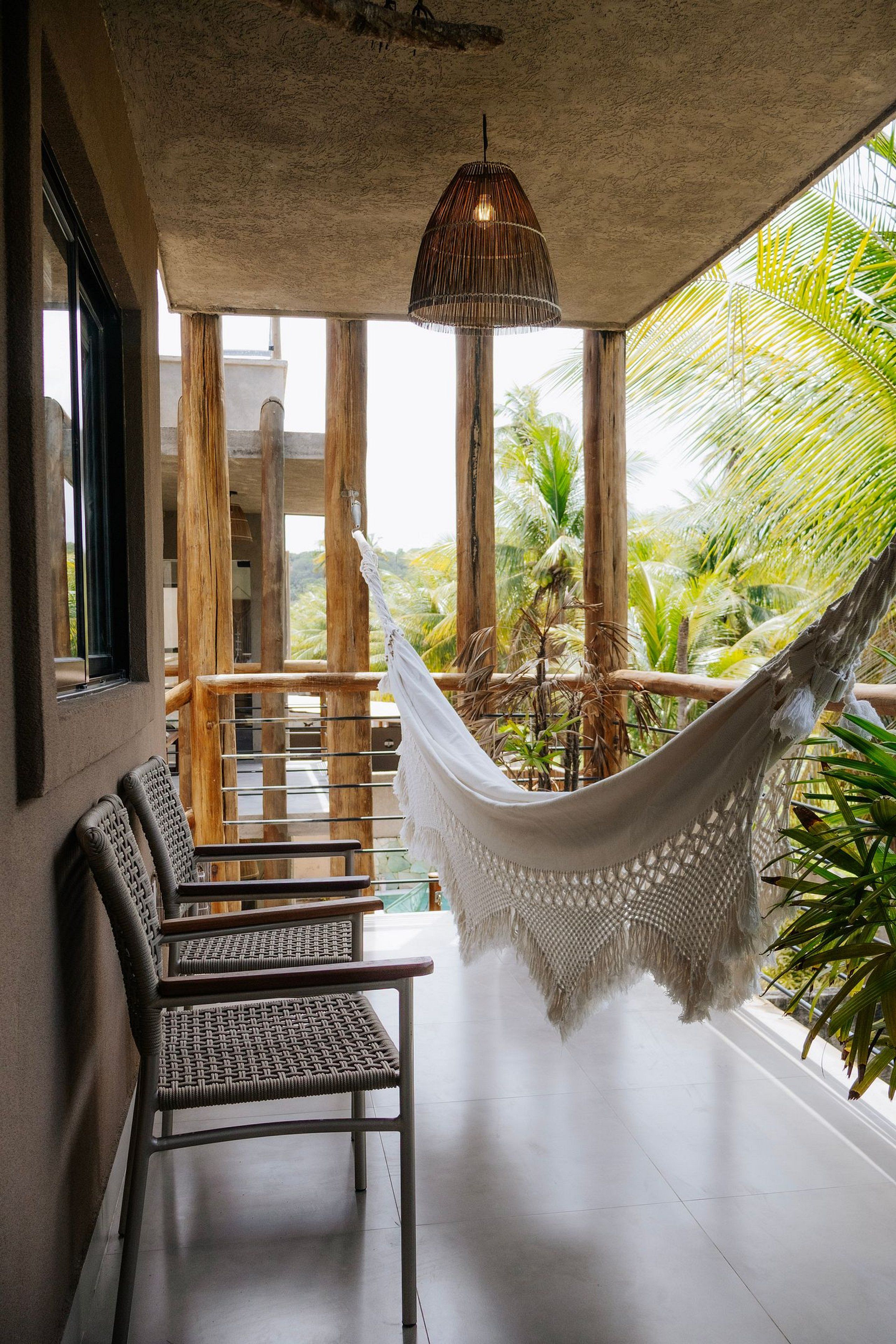 Una hamaca colgada de una estructura de madera, un espacio de descanso con sillas tejidas y vistas a plantas tropicales.