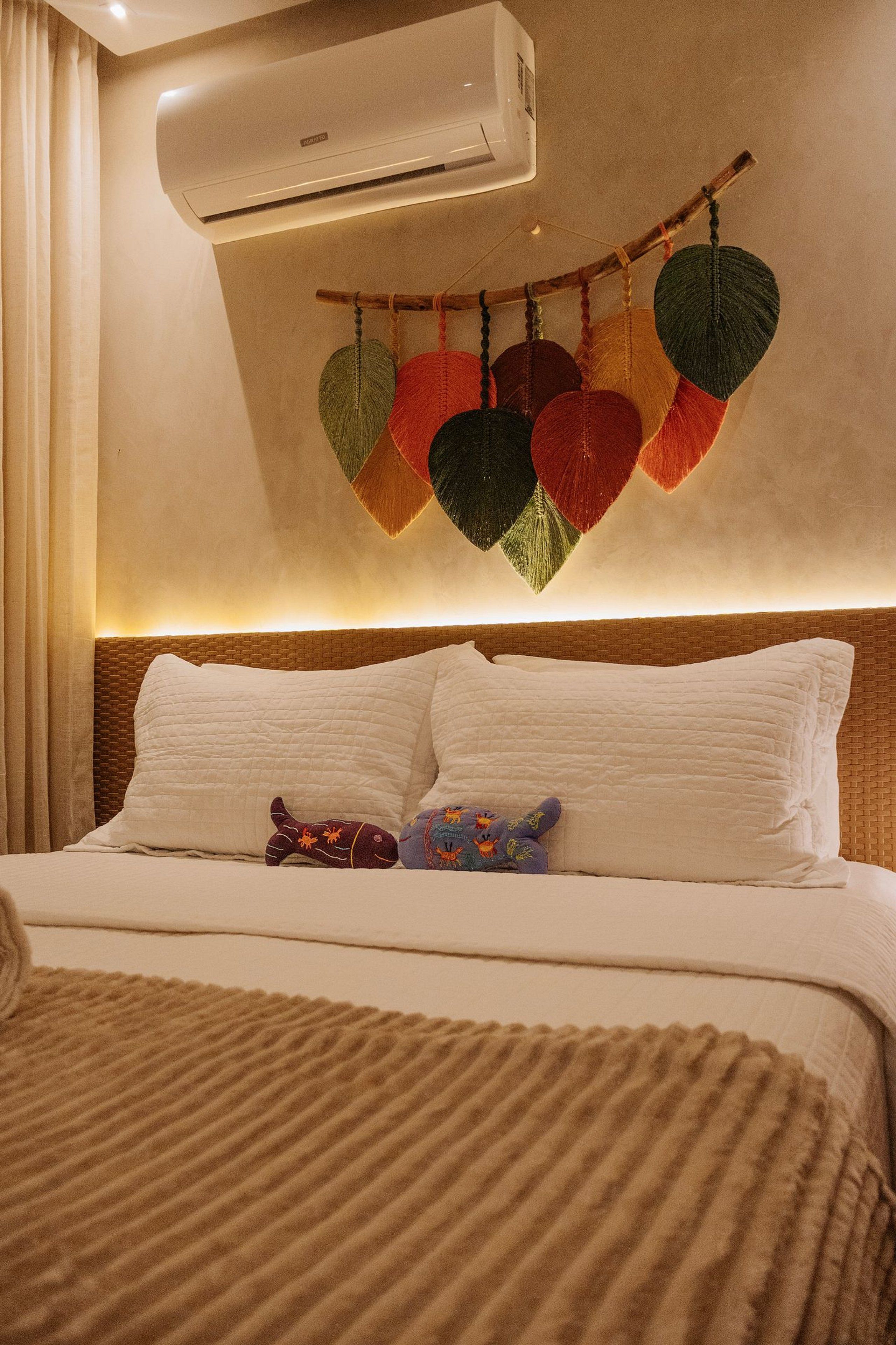 Quarto de hotel com cama, almofadas, ar condicionado fixado na parede e um ornamento pendente decorativo.