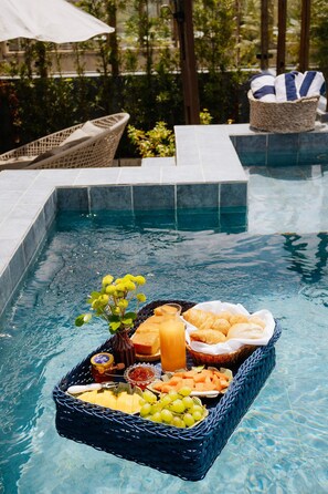 A poolside setting with a wicker basket containing food items like cheese, bread, and grapes. - Casa Deslumbrante a 3min a pe do mar (Sao Miguel dos Milagres)