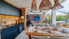 Una cocina moderna con horno empotrado, zona de comedor con mobiliario de mimbre y un televisor grande montado en la pared.