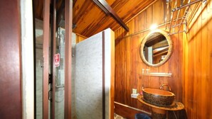 Interior de madera con cabina de ducha de vidrio, lavamanos de madera y espejo redondo, además de un suelo estampado.