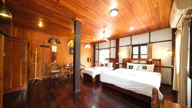 Habitación con paneles de madera, una cama, dos sillas, una mesa y un ventanal grande.