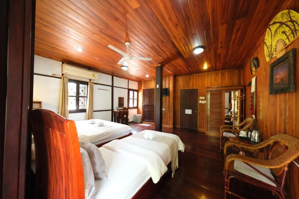 A room with wooden flooring, two beds with white linens, a ceiling fan, and a traditional Japanese-style wall decoration.