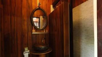 Un baño con paneles de madera, un espejo redondo, un lavamanos sobre pedestal y un inodoro.