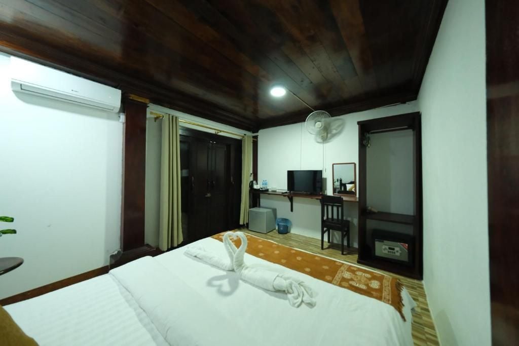 A hotel room with a bed, a desk with a computer, a TV, and a fan.