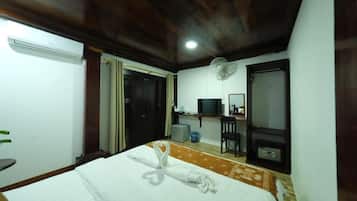 A hotel room with a bed, a desk with a computer, a TV, and a fan.