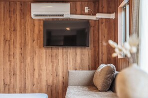 A room with a mounted air conditioner, a flat-screen TV, and a sofa with cushions. - Apartment Hotel 11 Tsutenkaku 3 (Osaka-shi)