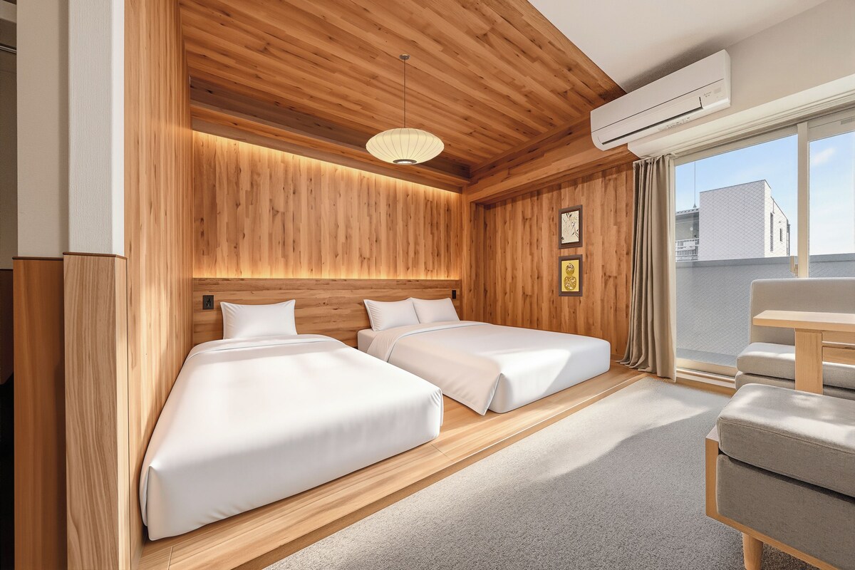 A hotel room with two beds, wooden paneling, a ceiling light, an air conditioning unit, and a view through a window.